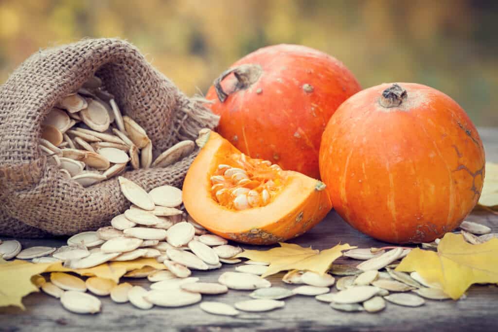 Zucche e borsa di tela con semi di zucca su tavola di legno.