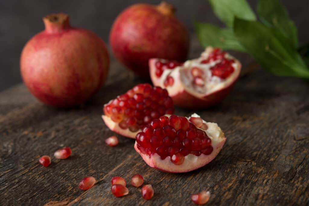melograno aperto con frutti esposti in da due melograni interi non aperti un tavolo di legno