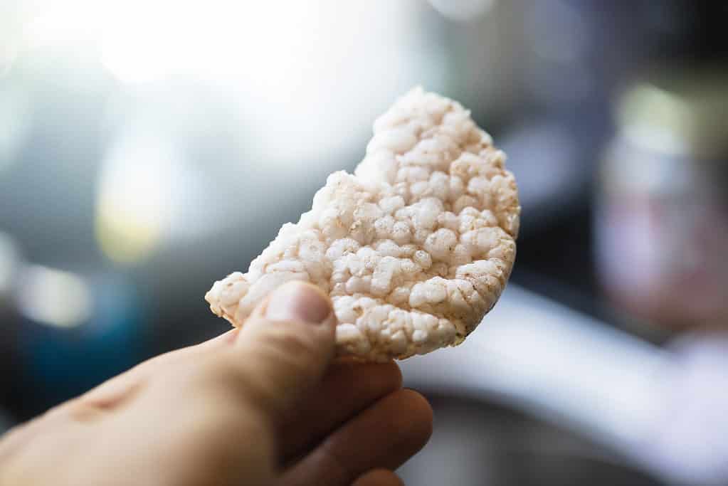 Torta di riso spezzata a metà, mano che tiene / dà cibo