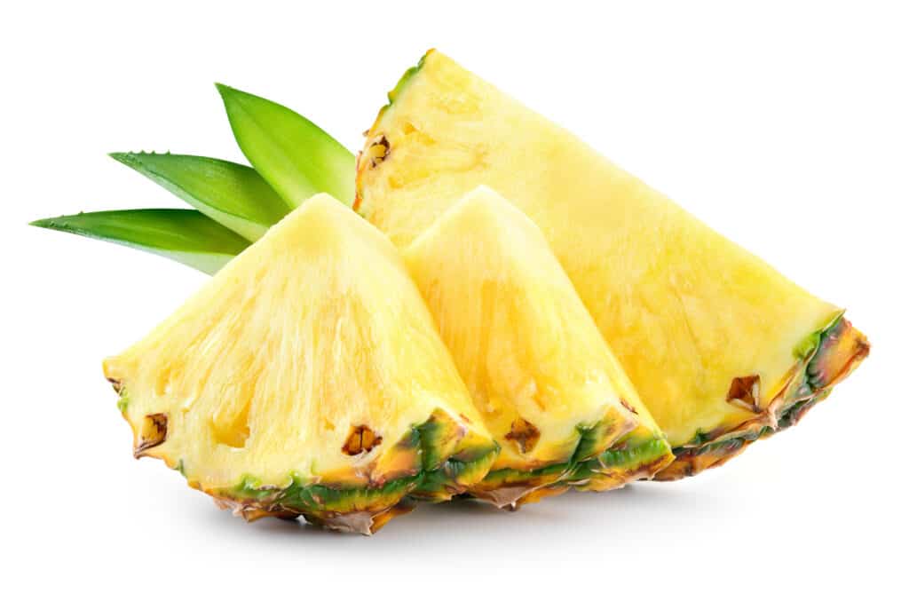 Cornice centrale: due spicchi triangolari di ananas fresco sono visti davanti a un cuneo tagliato a semicerchio.  con tre fronde di ananas contro l'isolato bianco.  La polpa dell'ananas è di colore giallo chiaro, buccia interna/buccia arancione/marrone.  con accenti verde scuro.  Le tre fronde (foglie) sono disposte insieme esteticamente.  Sono più verdi in punta, diventando più gialli più lontano dalla punta.