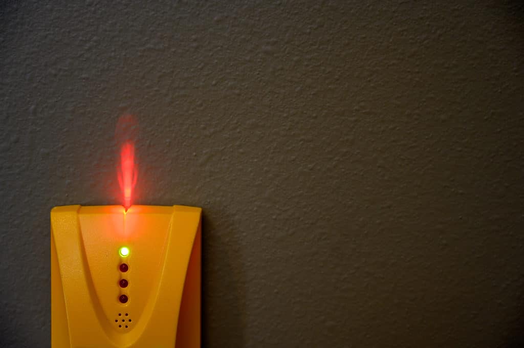 Lo sfondo è un muro isolato nero antracite: il riquadro in basso a sinistra è un mirino elettronico di plastica arancione brillante.  Ci sono quattro luci rotonde al centro del cercatore di perni, quella superiore è illuminata di verde.  Sotto le luci c'è un cerchio composto da sei piccoli fori con un piccolo foro al centro.  Una luce simile a una fiamma rossa brillante sta uscendo dalla parte superiore del mirino sulla parete nera come il carbone.
