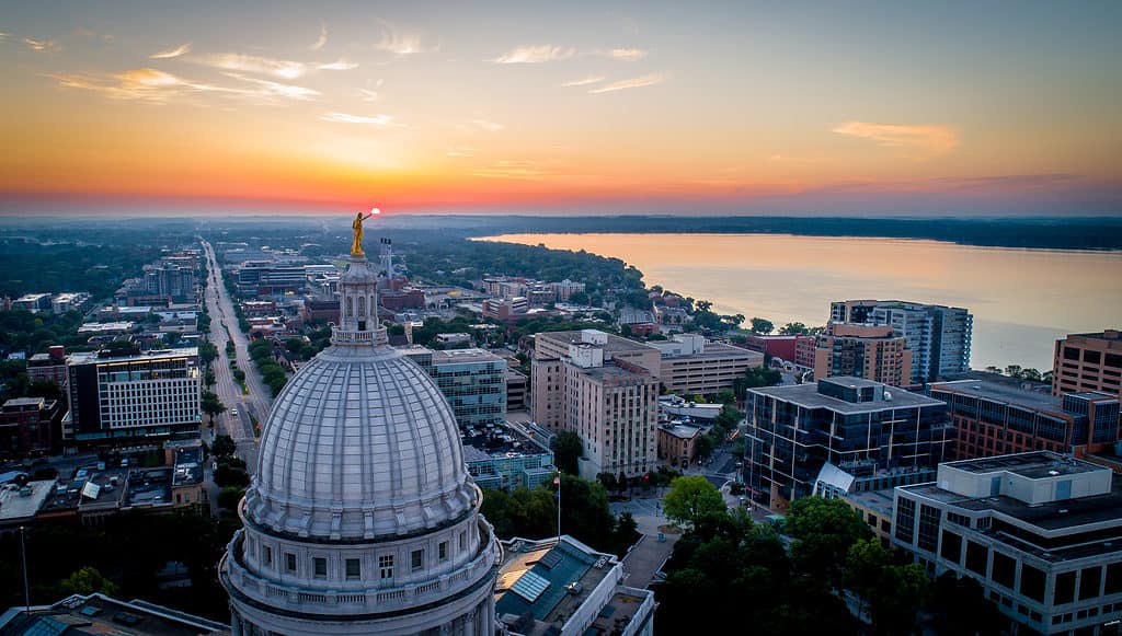 Ampia ripresa aerea di un'alba drammatica e infuocata sul Campidoglio dello stato del Wisconsin.  La statua in cima alla cupola sembra contenere il sole nascente.