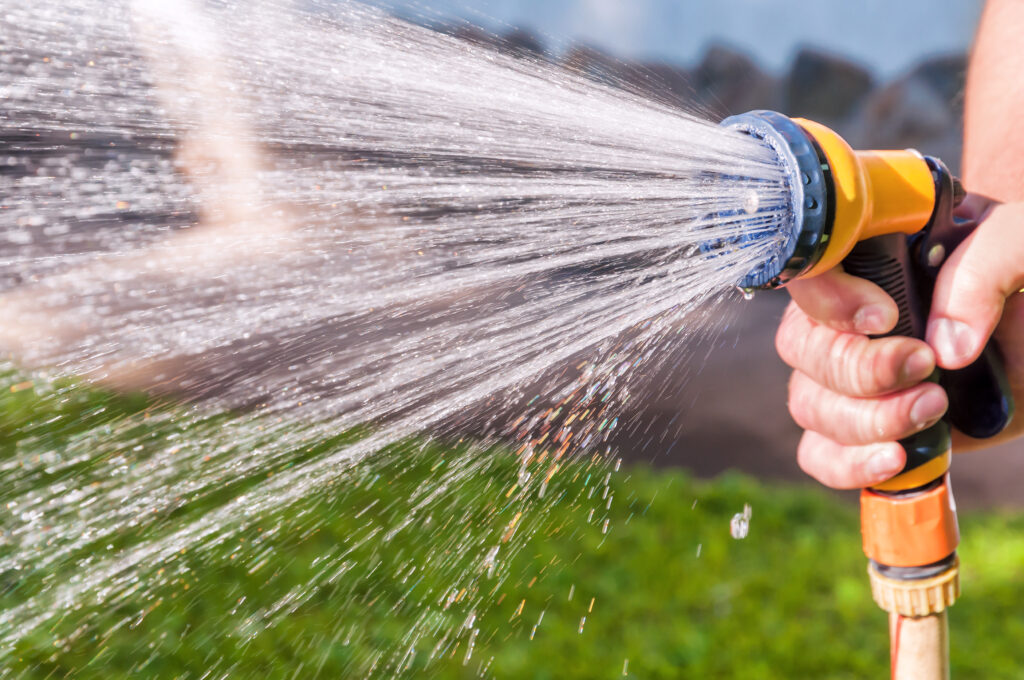 uomo con tubo dell'acqua che innaffia l'erba