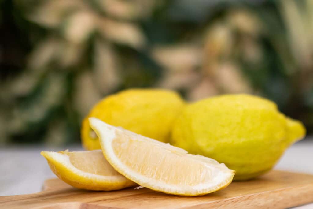 Due spicchi di limone Eureka su un tagliere di legno naturale con dietro due limoni Eureka interi e non affettati, con uno sfondo insignificante.