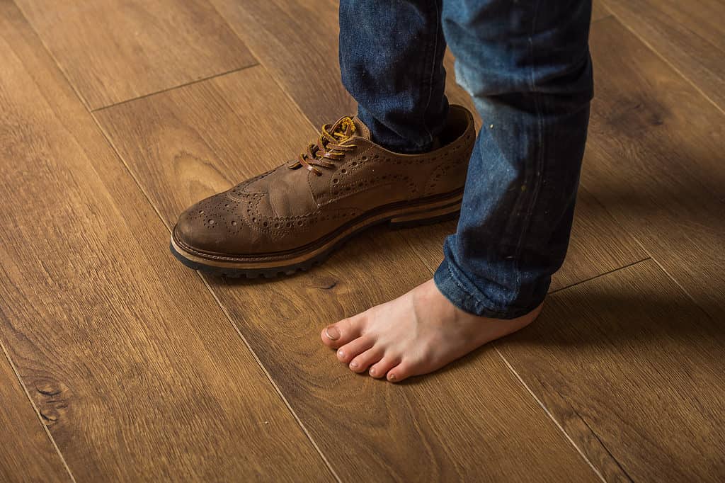 Bambino in scarpa grande su un piede in piedi sul pavimento. Il ragazzo divertente sogna di essere un grande uomo
