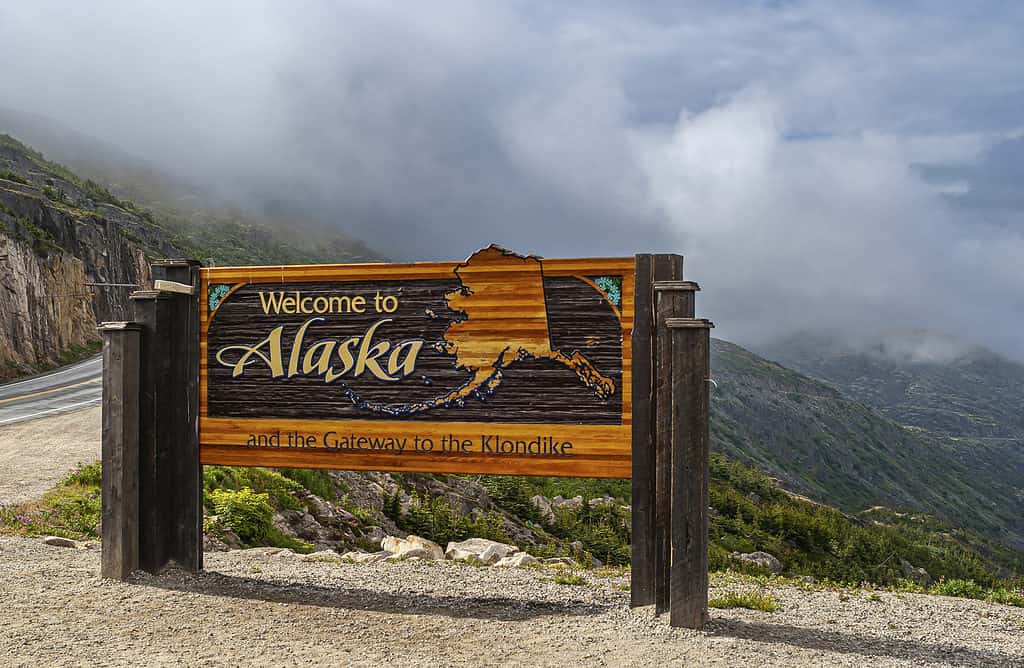 Skagway, Alaska, USA - 20 luglio 2011: Strada principale di Klondike al Canada.  Cartello di benvenuto colorato vicino al confine.  Cloudscape nella parte posteriore.