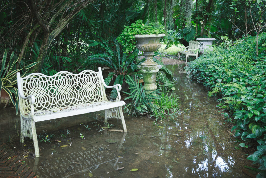 Sedia bianca in giardino all'aperto impregnato d'acqua, pieno di alberi e cespugli.