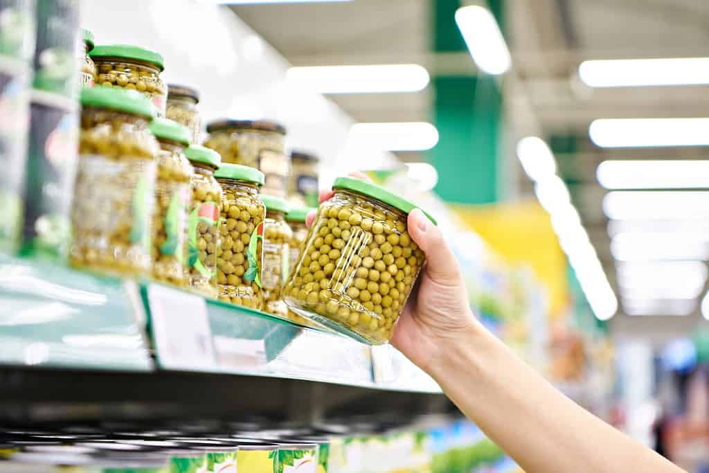 Piselli verdi in un barattolo di vetro nelle mani di un cliente in un negozio