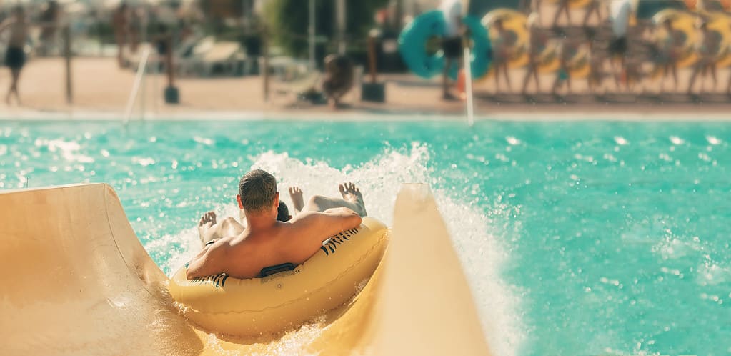 Persona in una camera d'aria che scivola lungo uno scivolo d'acqua in una grande area piscina