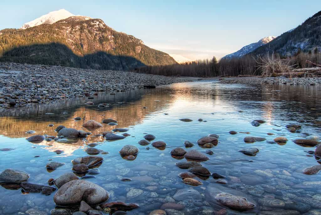 Il fiume limpido con le rocce conduce verso le montagne illuminate dal tramonto