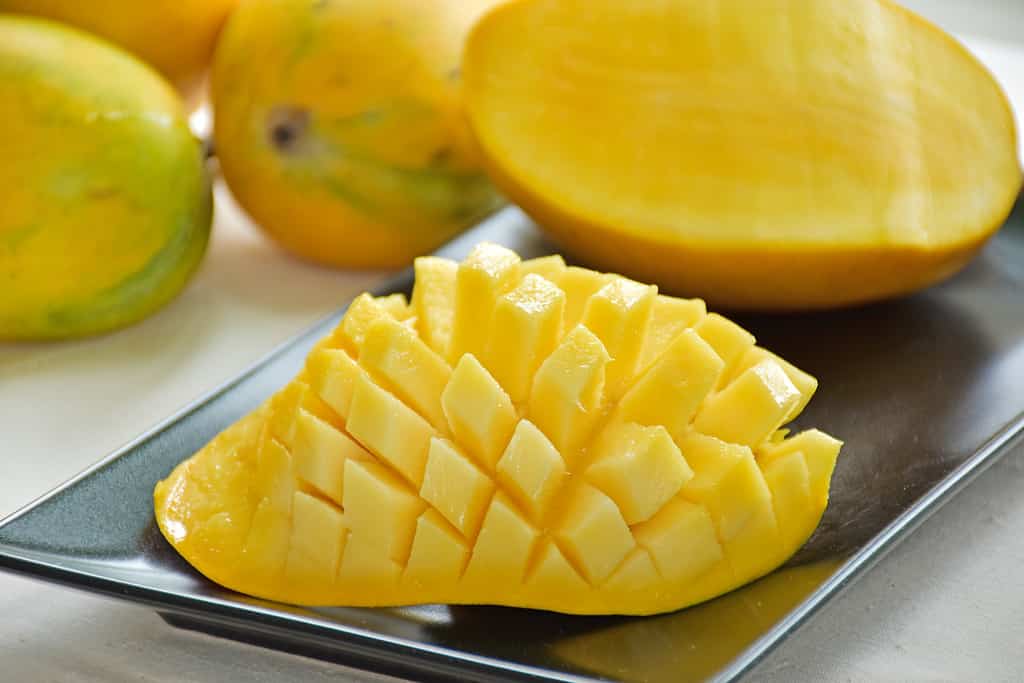 I mango al miele tagliati a metà.  I mango al miele tagliati a metà.  Famoso mango Bel taglio o carv isolare su sfondo bianco, immagine di messa a fuoco selettiva.  Sia la polpa che la buccia del mango sono gialle. 