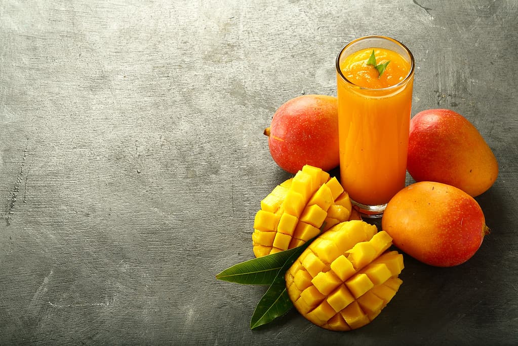 Alphonso mango, intero, affettato e come rinfrescante bicchiere di succo.  Tutto nella metà destra dell'inquadratura.