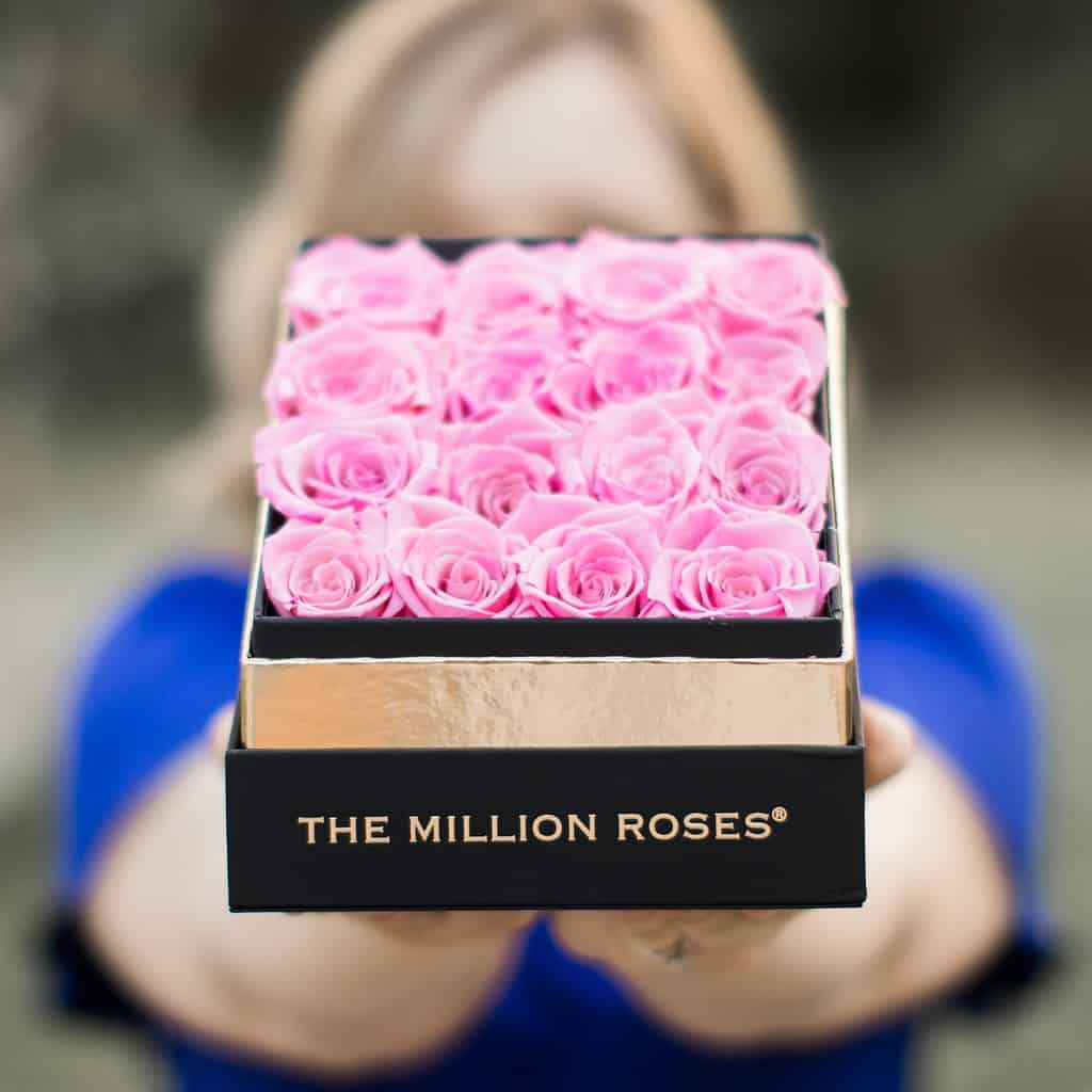 Una donna vestita di blu tiene in mano una scatola di rose rosa della Million Roses Company.