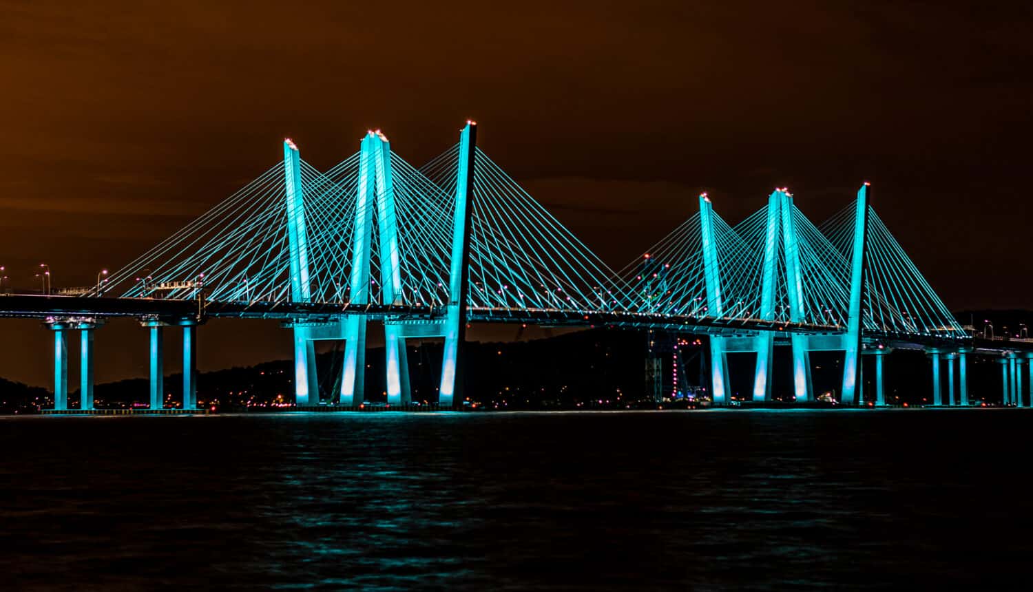 Vista del Governor Mario M. Cuomo Bridge (nuovo ponte Tappan Zee) di notte dal Pierson Park a Tarrytown, New York.  Il ponte è colorato in una bellissima tonalità verde blu con un cielo notturno infuocato.
