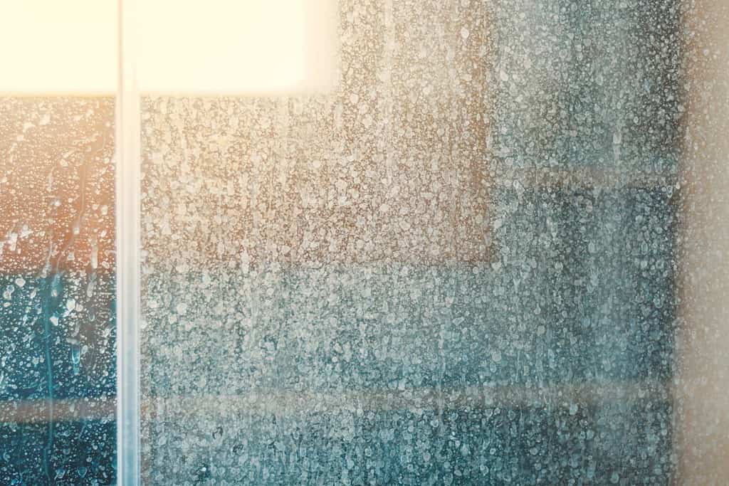 Rimozione di macchie e depositi di acqua dura in bagno.  Gocce di macchie sulle porte delle docce in vetro.  Concetto di pulizia del bagno.