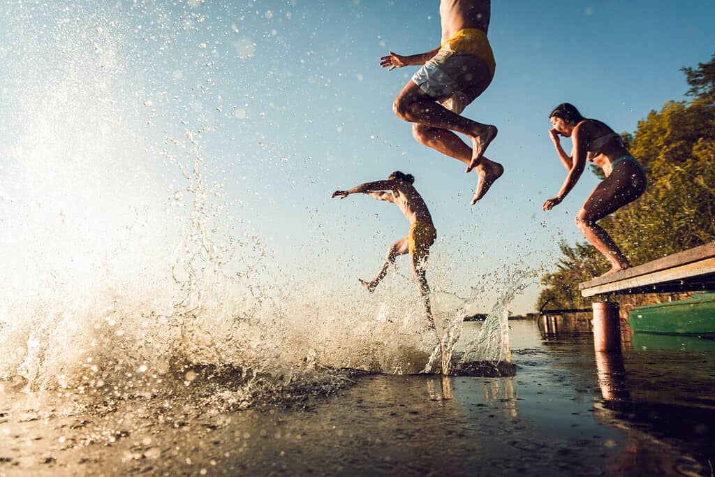 Amici che si divertono godendosi una giornata estiva nuotando e saltando nel lago.