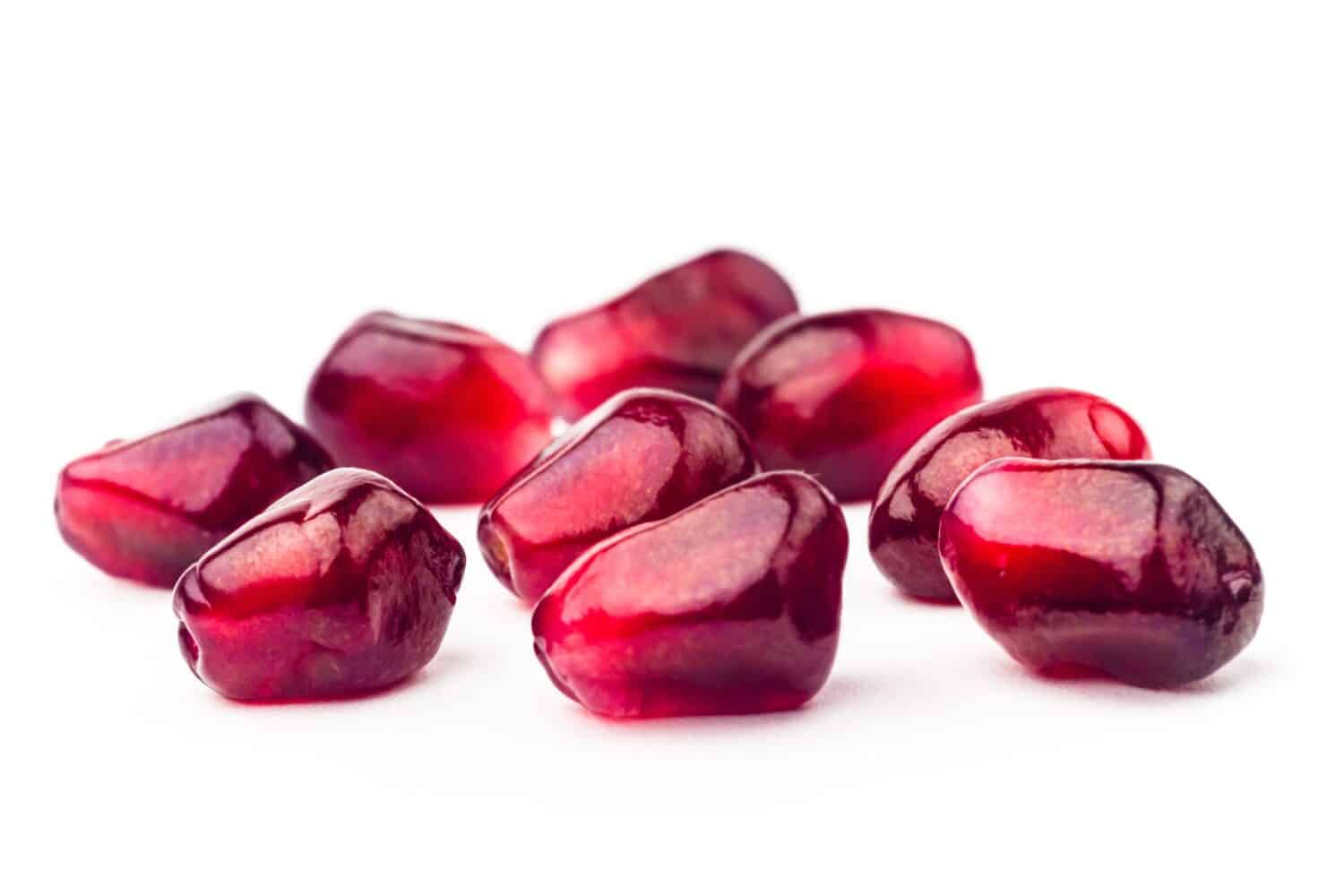 Semi di frutta granato con gocce d'acqua isolati su sfondo bianco.  Gruppo di semi di melograno primo piano.  Colpo a macroistruzione fresco dei grani del granato