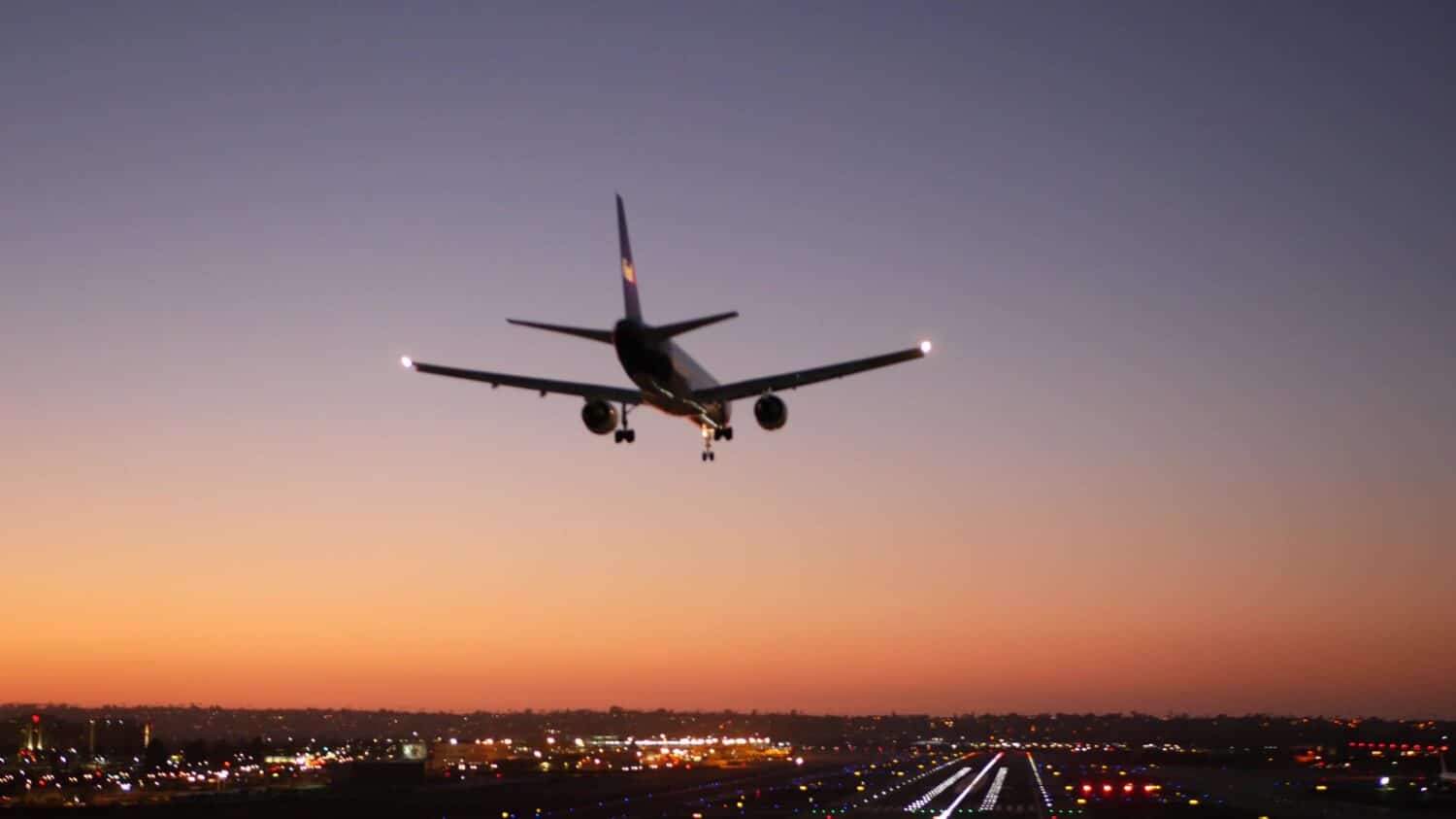 Luci della pista dell'aeroporto di notte, aereo o aereo che atterra sulla pista di atterraggio, crepuscolo e tramonto. Jet aereo di linea che arriva all'aerodromo, campo d'aviazione di San Diego, California USA. Aerei che volano a mezz'aria nel cielo.