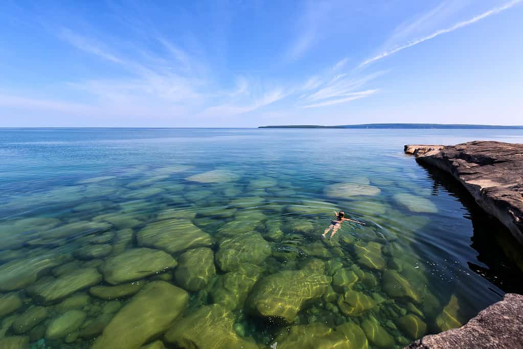 Una ragazza nuota nel Lago Superiore nella penisola superiore del Lago Michigan. Le rocce sono visibili attraverso il vetro come acque incontaminate. Nella foto Rocks National Lakeshore è in lontananza.