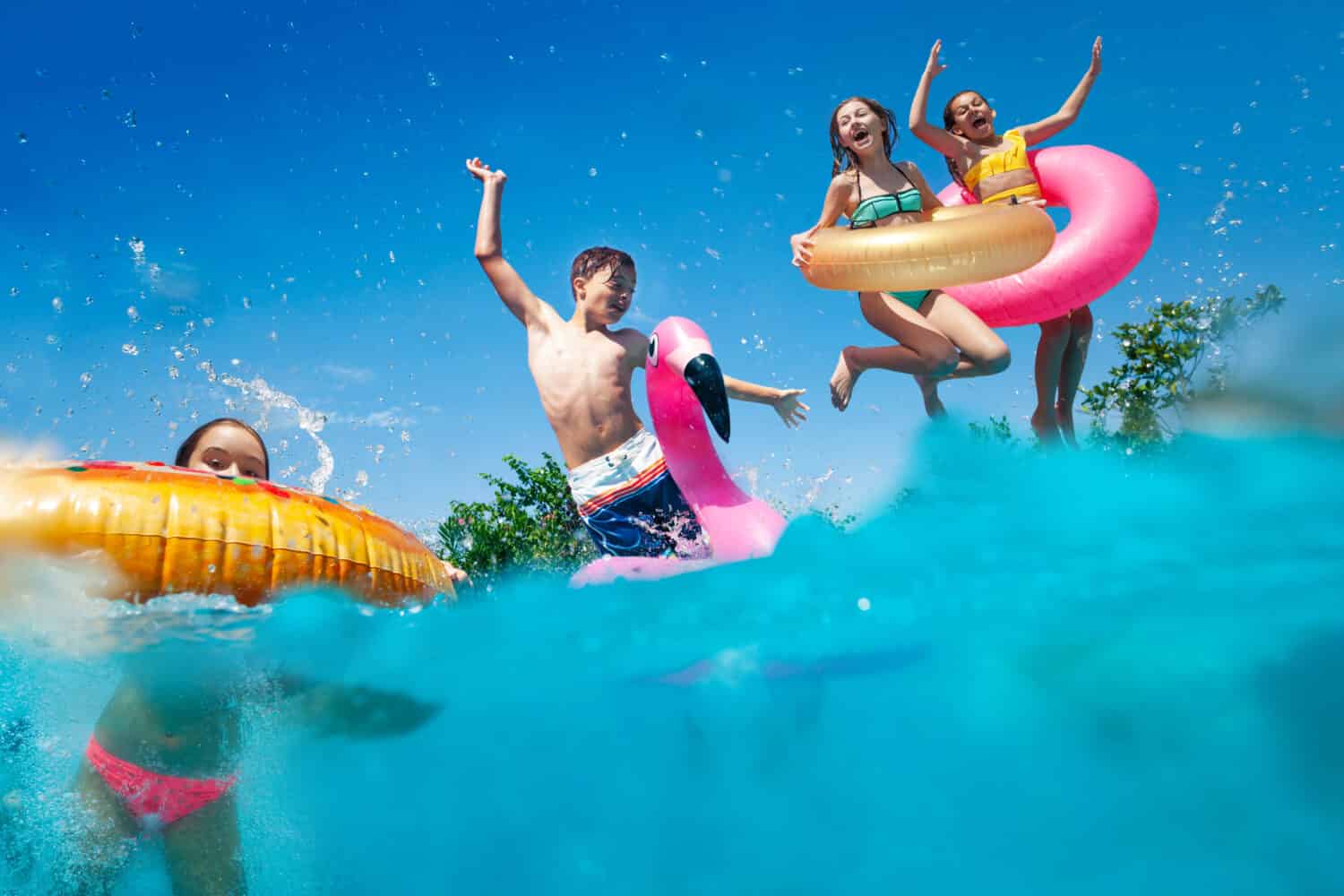 L'immagine divisa a metà sott'acqua di molti bambini piccoli si tuffa in piscina lanciando giocattoli gonfiabili che alzano le mani si divertono
