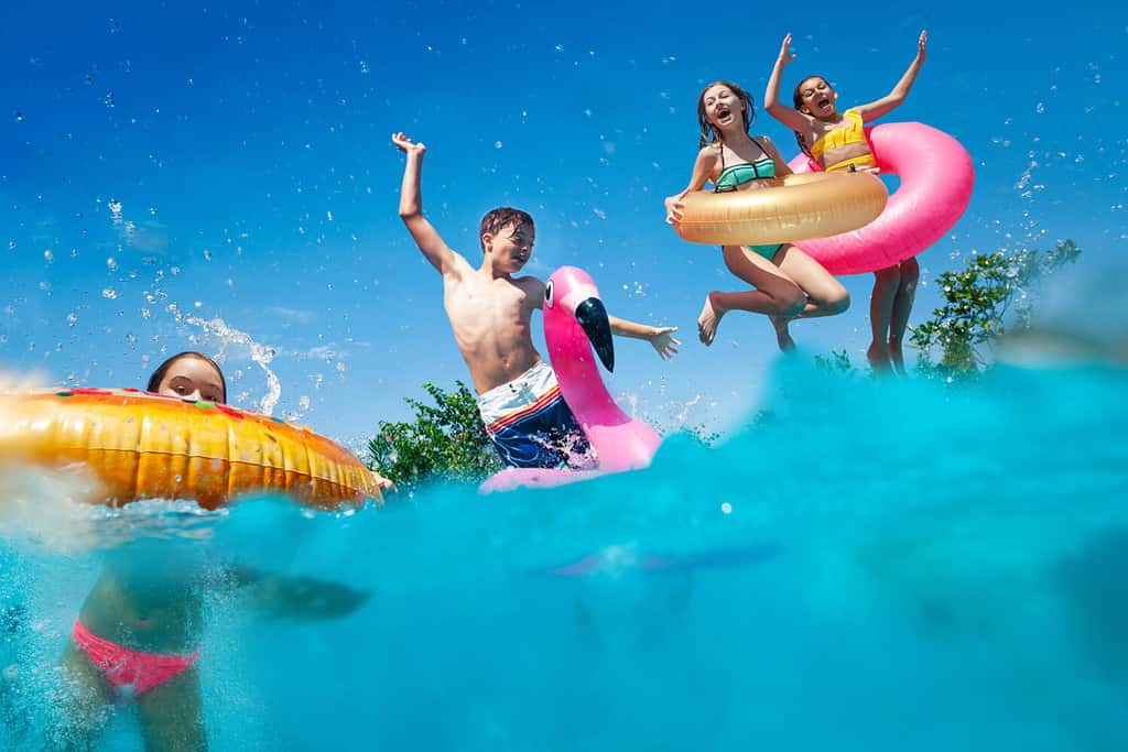 L'immagine divisa a metà sott'acqua di molti bambini piccoli si tuffa in piscina lanciando giocattoli gonfiabili che alzano le mani si divertono
