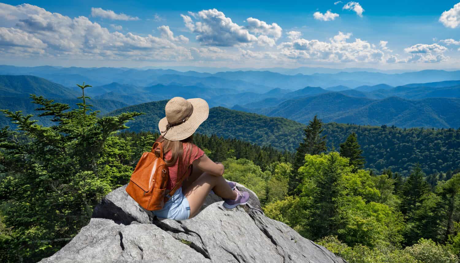 Ragazza della viandante che si siede su un bordo della scogliera che gode della vista panoramica di estate. Donna che si rilassa in cima alla montagna autunnale, sopra le nuvole. Blue Ridge Parkway ,vicino a Asheville, North Carolina, Stati Uniti d'America.