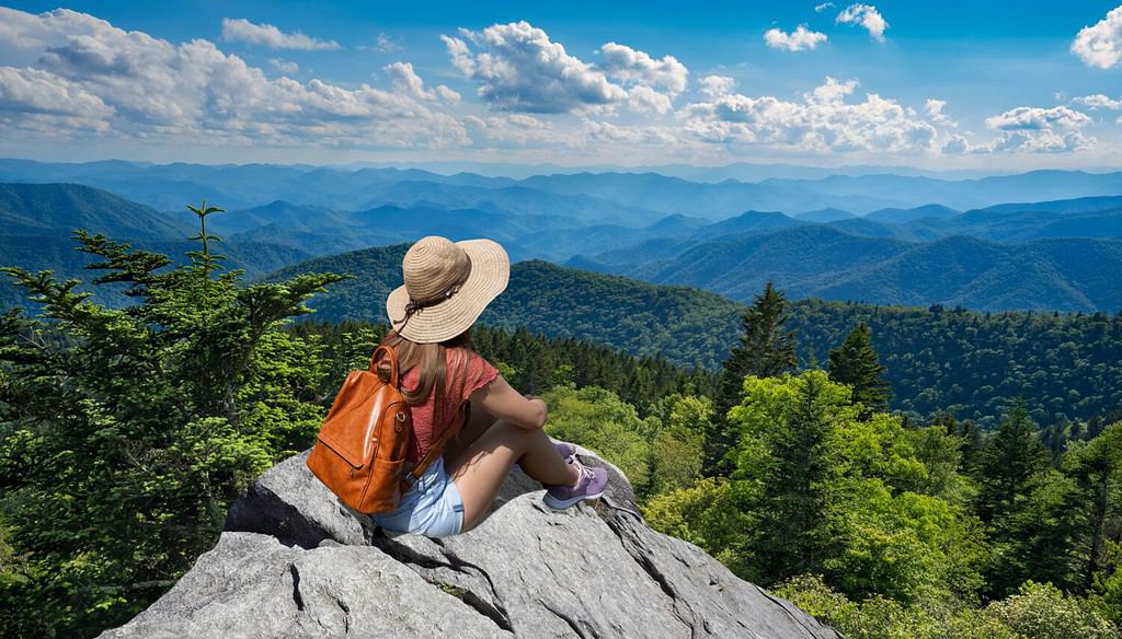 Ragazza della viandante che si siede su un bordo della scogliera che gode della vista panoramica di estate. Donna che si rilassa in cima alla montagna autunnale, sopra le nuvole. Blue Ridge Parkway ,vicino a Asheville, North Carolina, Stati Uniti d'America.