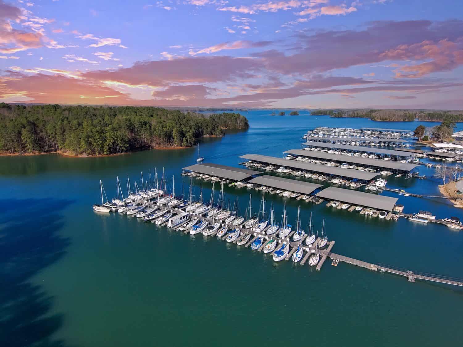 Barche e yacht attraccati e navigano nel porto turistico sul lago Lanier con lussureggianti alberi verdi e potenti nuvole al tramonto a Cummings Georgia USA