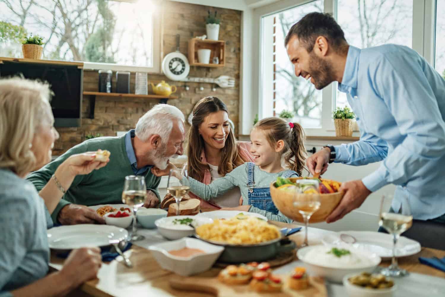 Felice famiglia di più generazioni che si riunisce attorno al tavolo da pranzo e si diverte durante un pranzo.