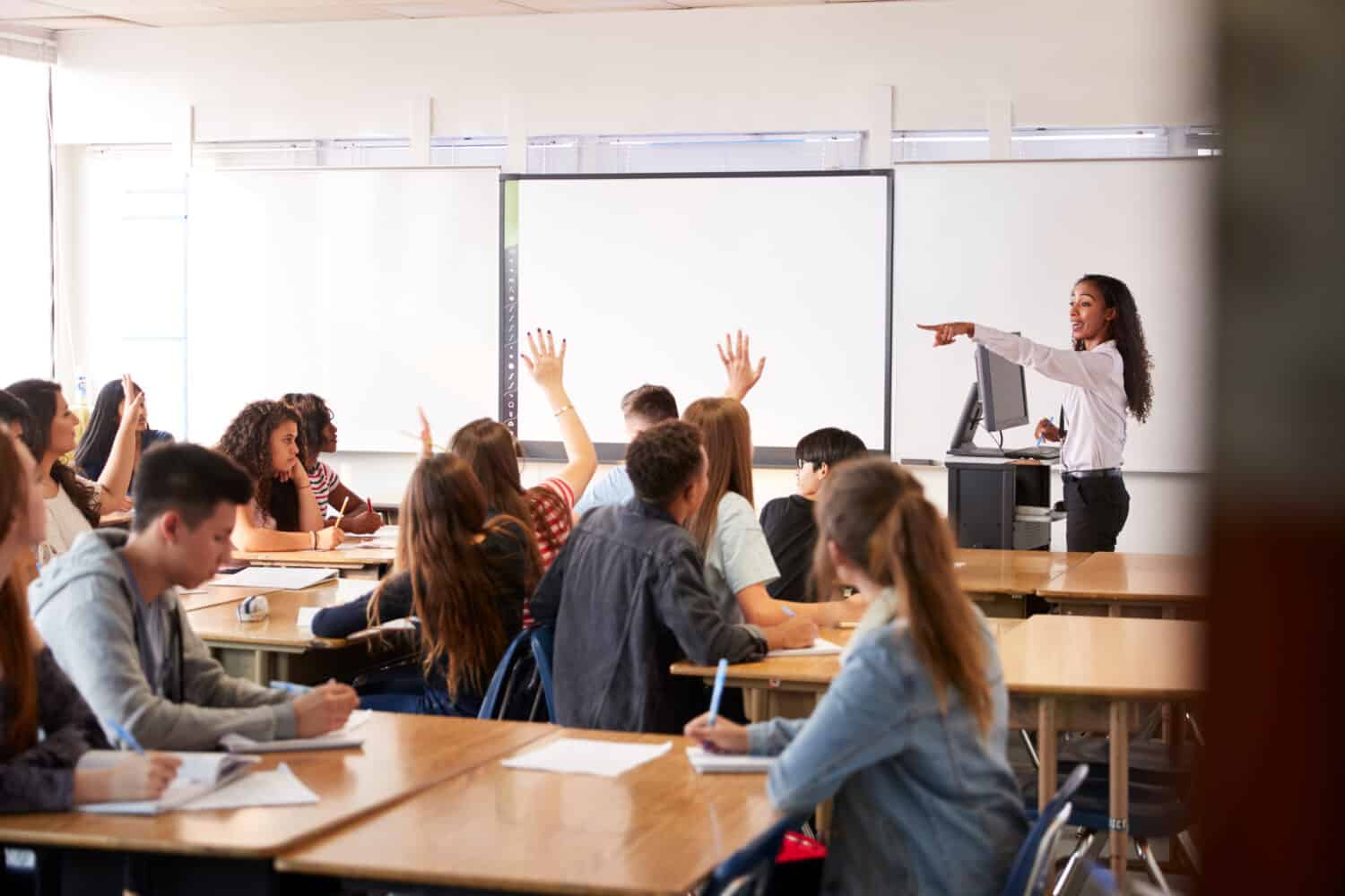 Insegnante di scuola superiore femminile che fa domanda in piedi accanto alla lezione di insegnamento della lavagna interattiva
