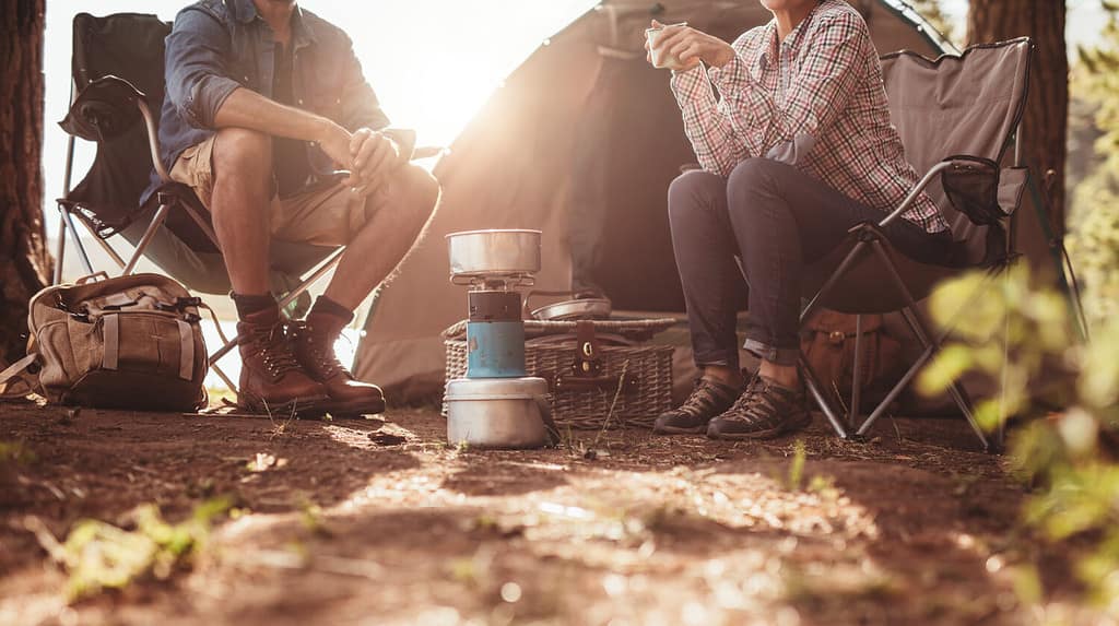 Immagine ritagliata di un uomo e di una donna seduti su sedie fuori dalla tenda. Coppia campeggio nella foresta.