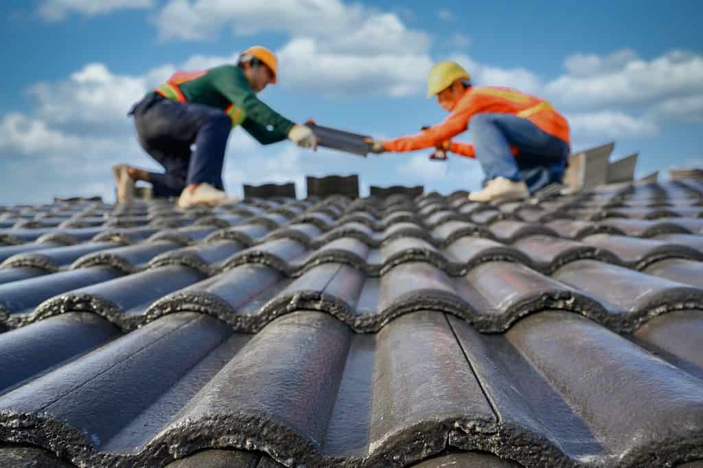 Seleziona il focus sulle tegole. Sfondo sfocato di un roofer che lavora sul tetto di una casa Utilizzare un trapano per forare le viti per fissare le tegole di cemento.