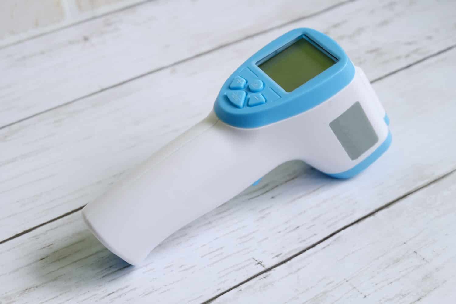 Termometro a infrarossi senza contatto su fondo di legno bianco per misurare la temperatura corporea.  Tema sanitario e medico.