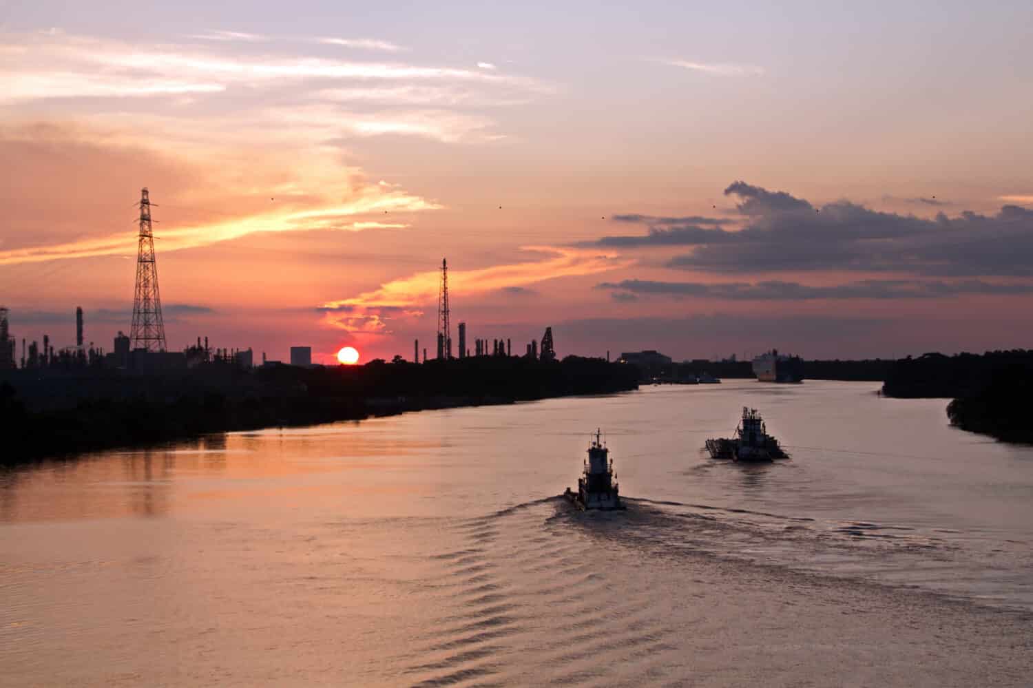 Vista panoramica dell'argine e della costa sul fiume durante il giorno e la sera contro il cielo blu, le nuvole e i raggi del tramonto. Fiume Neches.  Port Beaumont, Texas, USA.Luglio 2017.