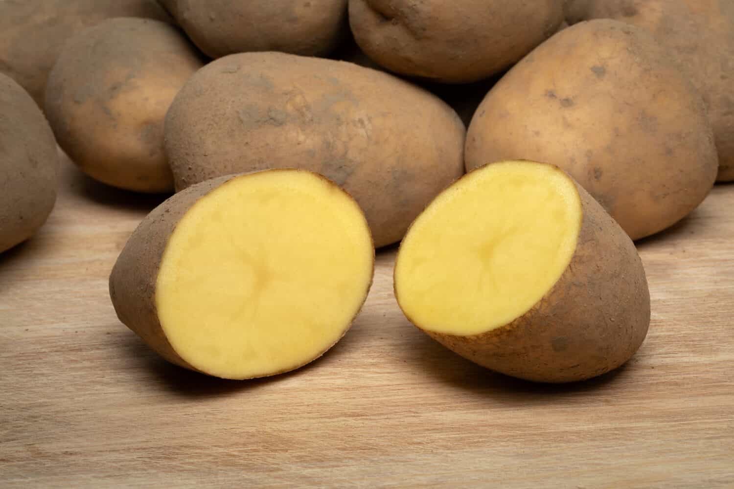 Patate di varietà olandese chiamate Bintje intere e dimezzate su sfondo di legno da vicino 