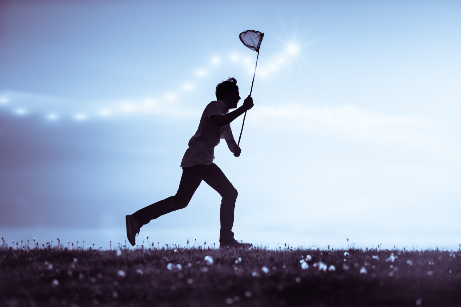 Giovane che cattura insetti al tramonto che corre lungo l'orizzonte che si staglia contro un cielo blu nuvoloso brandendo la sua rete