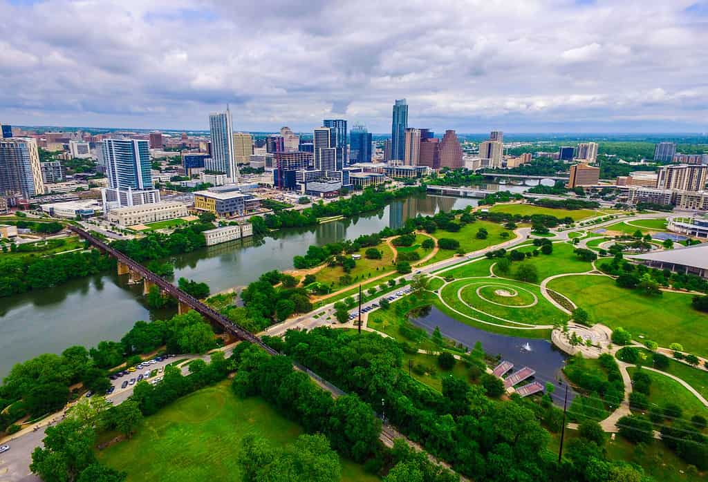 Aerea sopra Austin Texas, colori primaverili con binari ferroviari che attraversano il lago Lady Bird allo Zilker Park e l'Auditorium Shores con il paesaggio urbano dello skyline e il centro sullo sfondo a nord del fiume