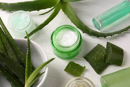 Diversi prodotti cosmetici e foglie di aloe vera tagliate su tavolo di legno bianco, sopra la vista