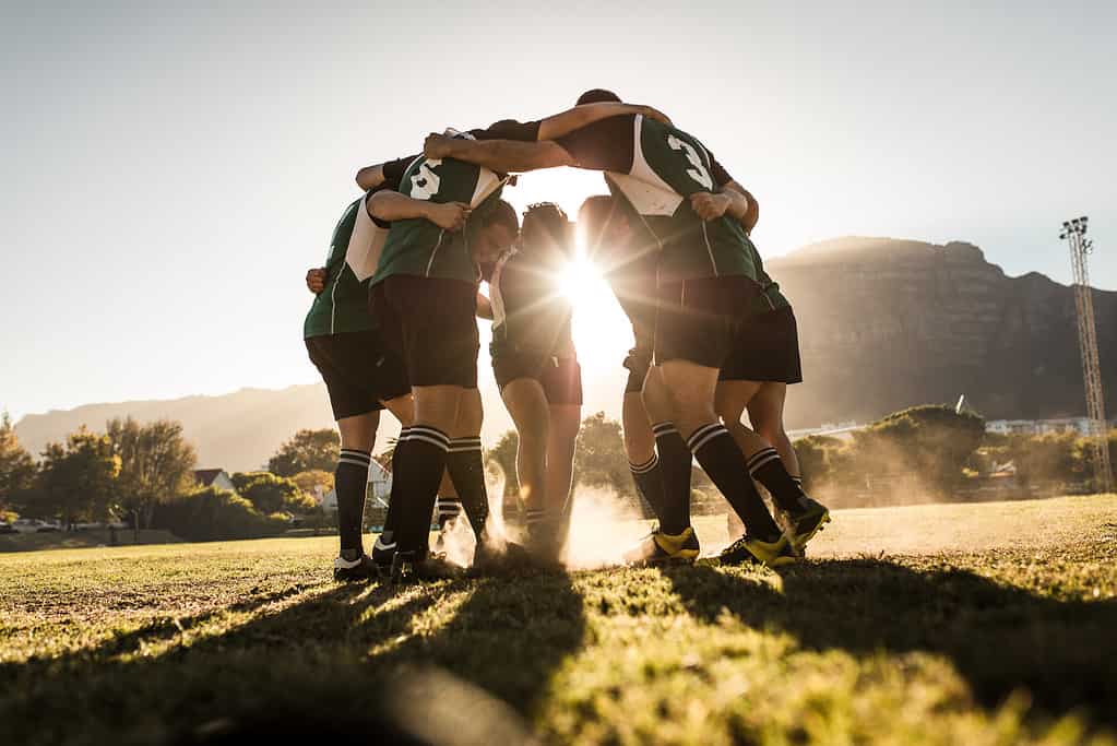 Squadra di rugby in piedi in una calca e strofinando i piedi a terra.  Squadra di rugby che celebra la vittoria.
