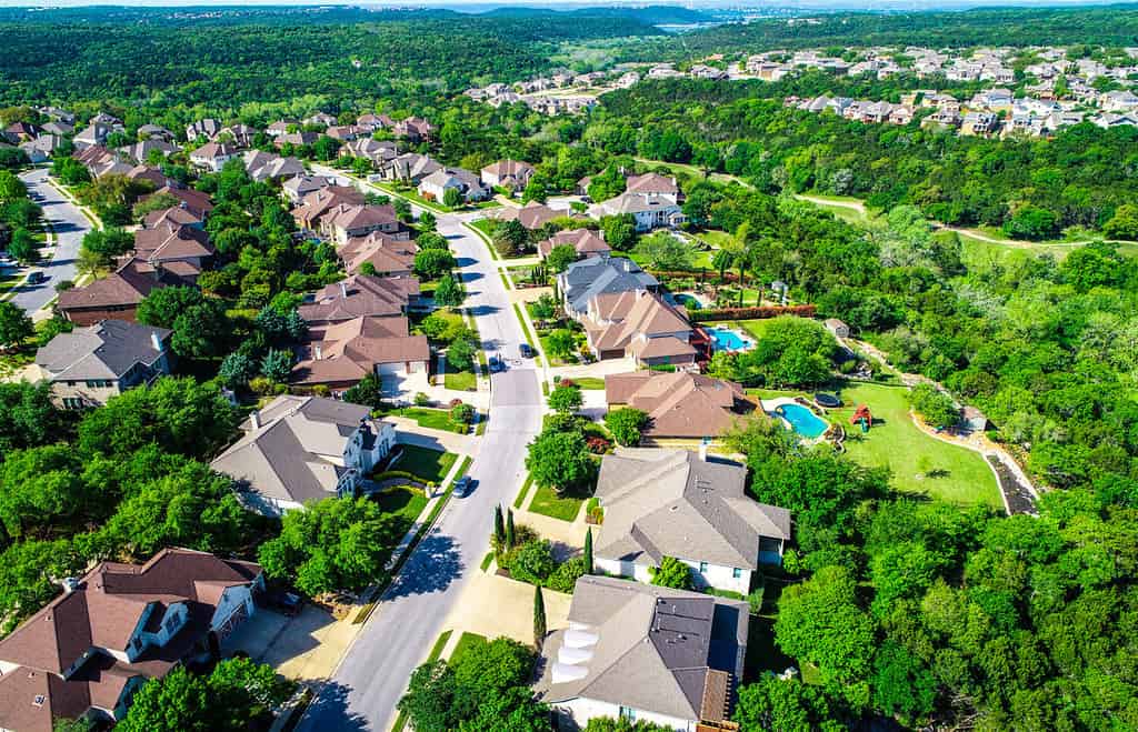 Vista aerea del drone sopra la strada curva con case di lusso che conducono al verde paesaggio collinare del Cedar Park Texas Suburb