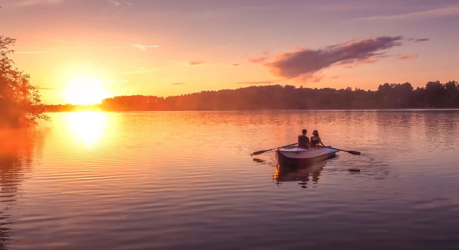 Un bellissimo tramonto dorato sul fiume. Gli innamorati vanno in barca su un lago durante uno splendido tramonto. Coppia felice donna e uomo insieme rilassanti sull'acqua. La bellissima natura intorno.