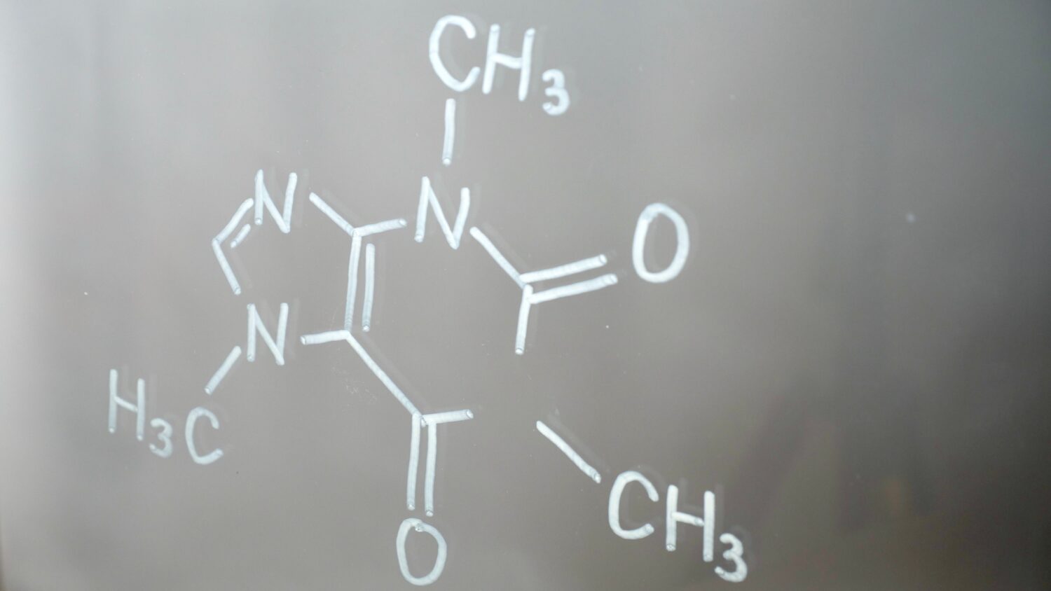 Struttura chimica, formula della caffeina sul vetro in primo piano in laboratorio.  Mostra gruppi amminici e ammidici funzionali.