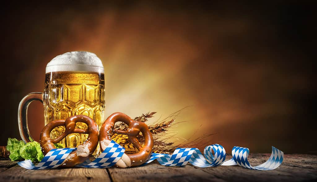 Birra Oktoberfest con pretzel, frumento e luppolo su tavolo di legno