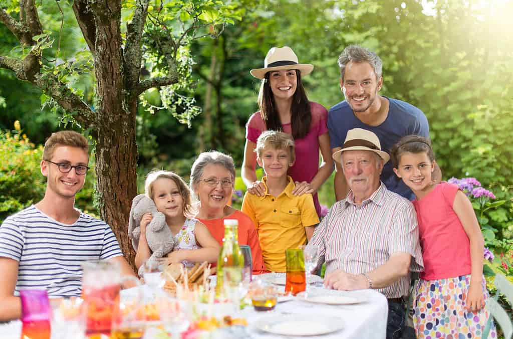 In estate, riunione di famiglia attorno a un tavolo da picnic in uno splendido giardino. Tutte le generazioni posano per la macchina fotografica. Girato con bagliore