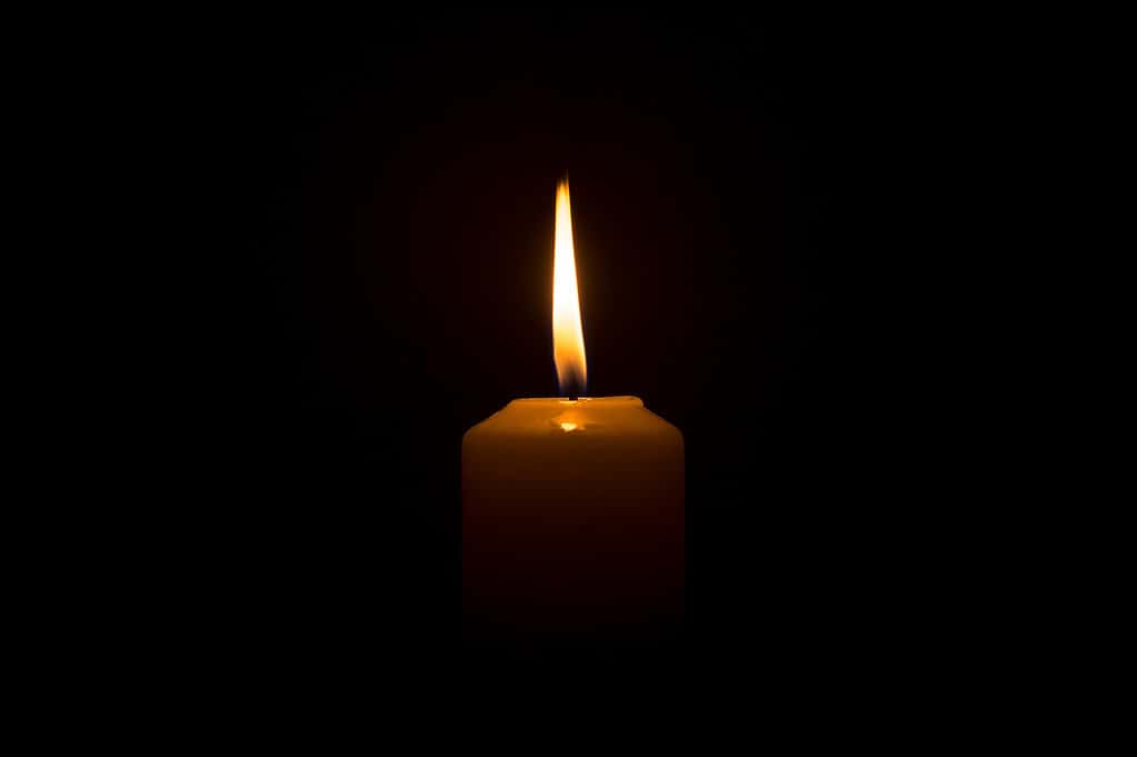 Una singola fiamma di candela accesa o una luce che brilla su una candela bianca su uno sfondo nero o scuro sul tavolo in chiesa per Natale, funerali o servizi commemorativi