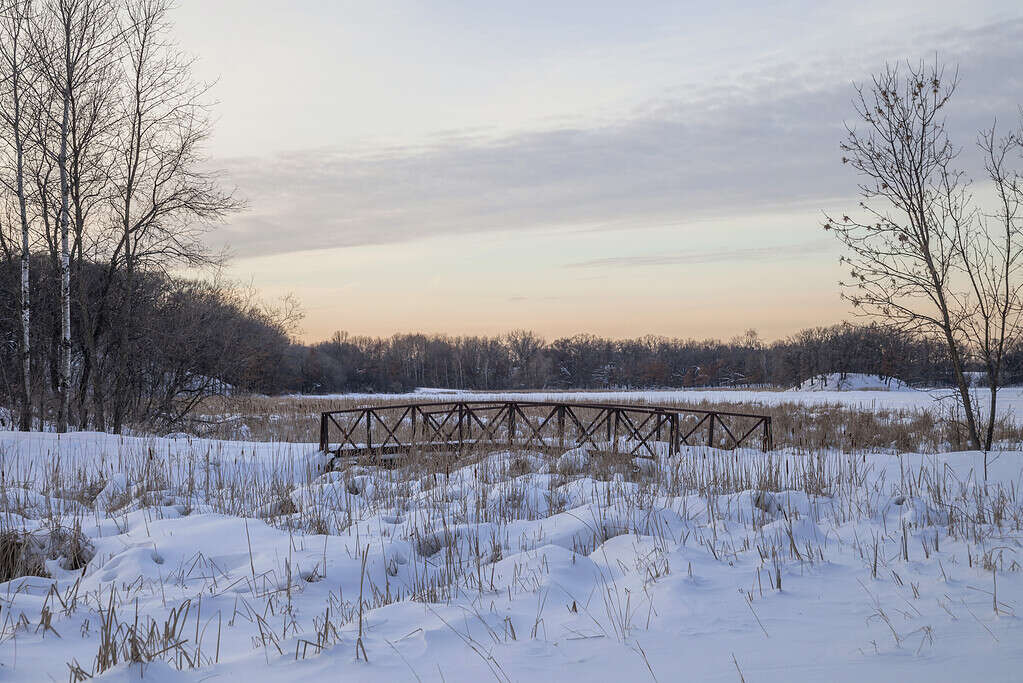 Un ponte pedonale in un paesaggio innevato durante un tramonto invernale