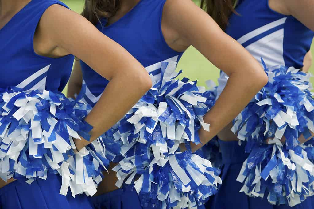 Tre cheerleader in uniforme blu e bianca e pompon