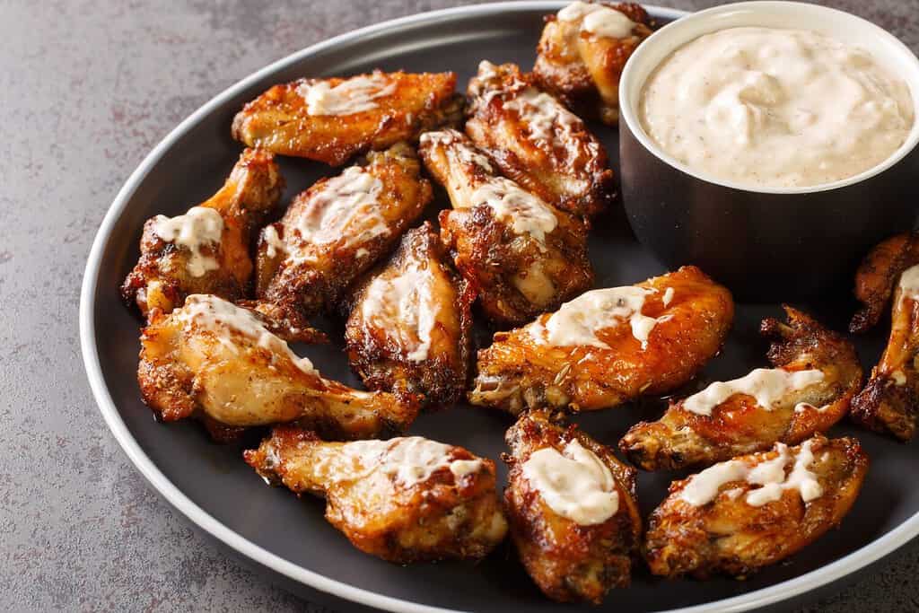 Ali di pollo alla griglia americane con salsa barbecue bianca dell'Alabama in un piatto sul tavolo. Orizzontale