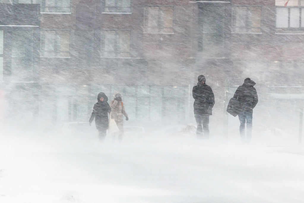 La bufera di neve, il forte vento, il nevischio, sullo sfondo delle case sagome sfocate di persone, cercano di nascondersi dal maltempo, superano tutte le difficoltà del clima rigido. vai alla fermata dell'autobus.