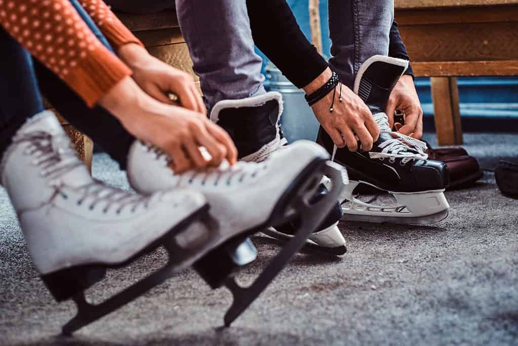 Giovani coppie che si preparano ad un pattinaggio. Foto ravvicinata delle loro mani che allacciano i lacci delle scarpe dei pattini da hockey su ghiaccio nello spogliatoio